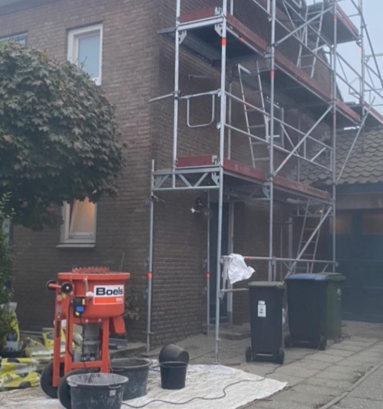 Bouwsteiger naast huis met bouwmaterialen en gereedschap.